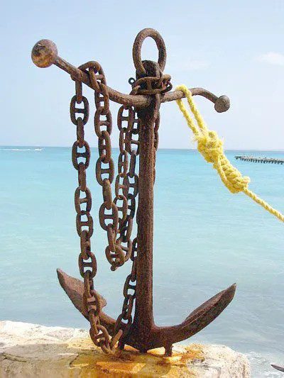 Ship anchor on the ground with a chain hanging on it and a rope tied to it