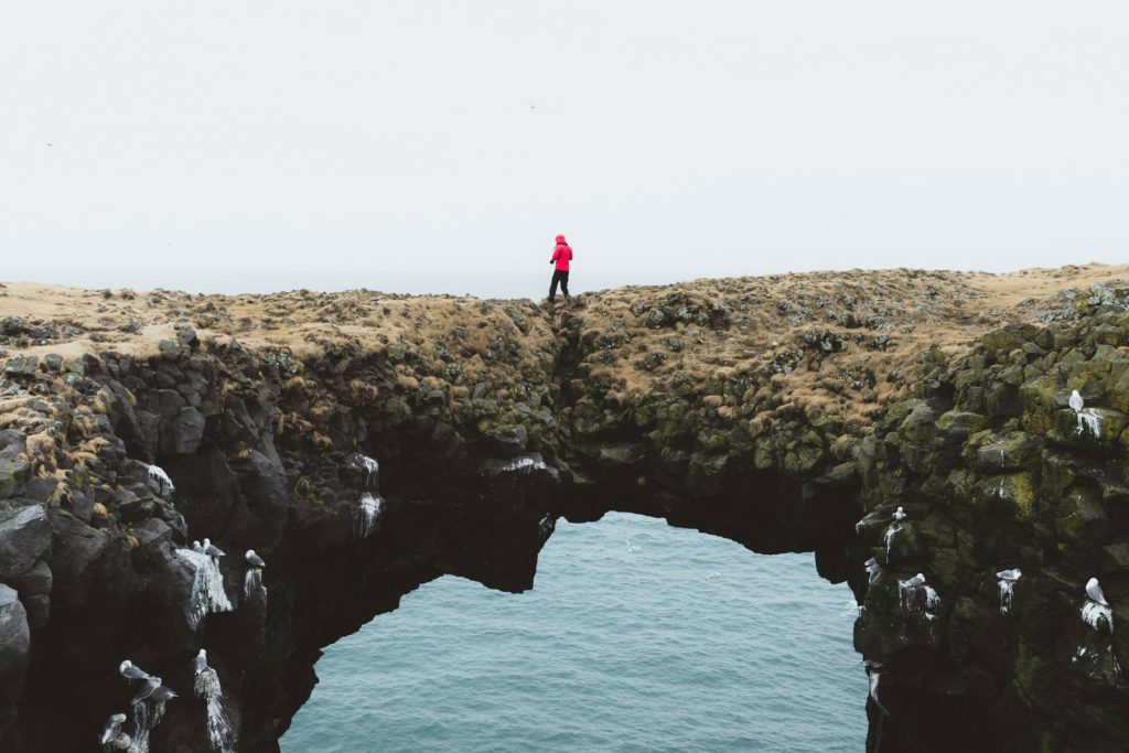 Person standing on rock arch over water