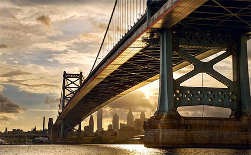 Bridge over water at sunset with city skyline in the back